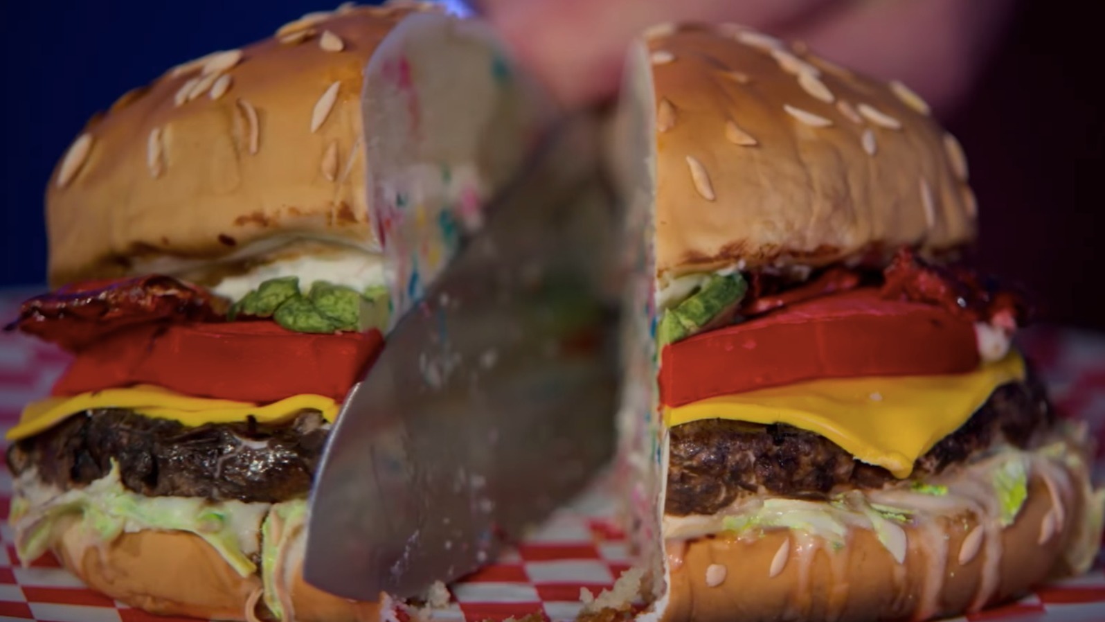 A knife cutting through a burger cake in Is It Cake?