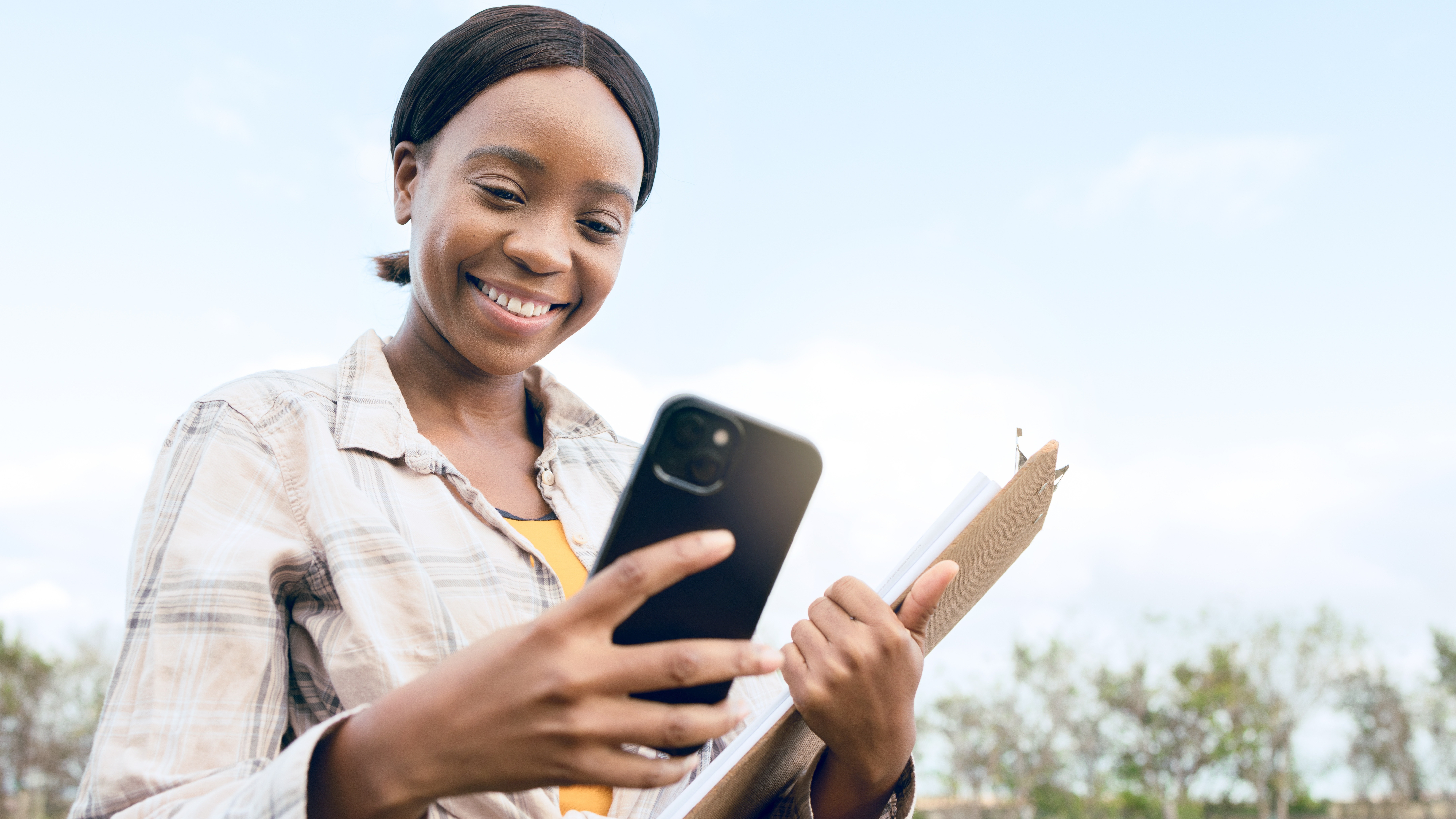 Woman holding iPhone and clipboard in a field