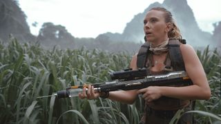 Zora holding a rifle and looking up as she stands in some tall grass in Jurassic World: Rebirth