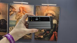 Man holding up the iFi iDSD GR 2 in front of artwork