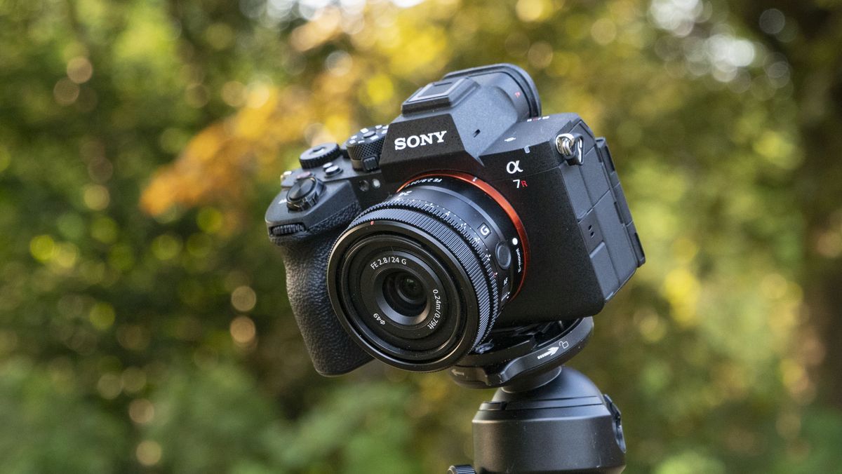 The Sony A7R VI camera with 24mm f/2.8 lens attached, it's mounted to a tripod outdoors, there's a natural background