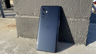 A OnePlus 9 from the back, leaning against a brick pillar