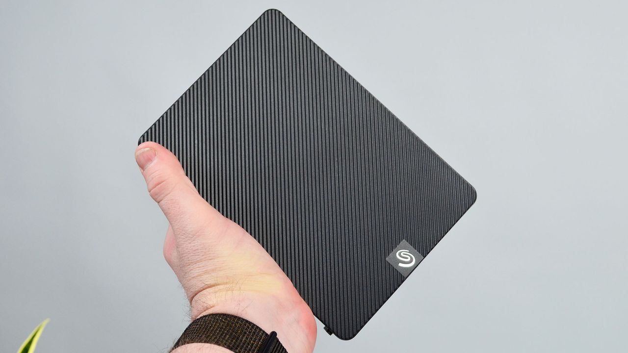 A masculine hand holding a Seagate Expansion external desktop hard drive