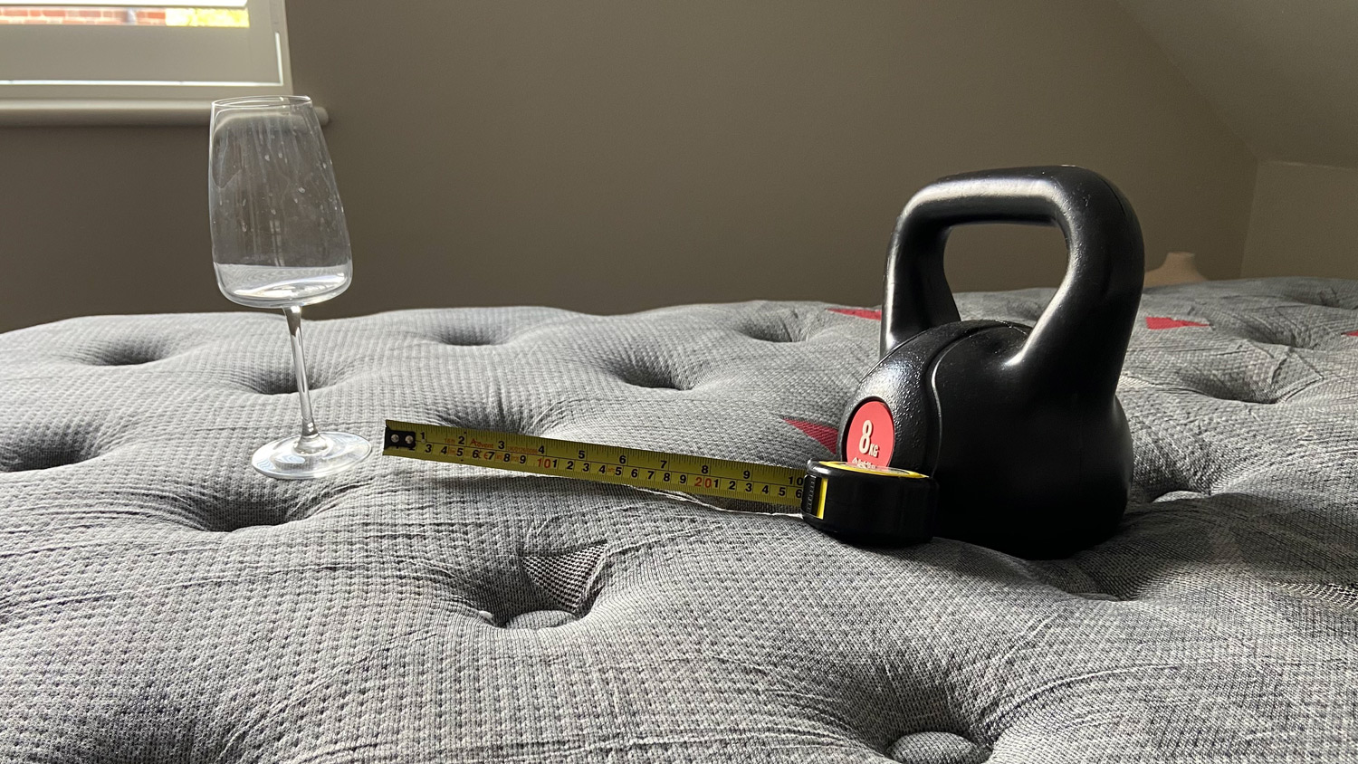 A wine glass, weight and tape measure on the Zoma Boost mattress