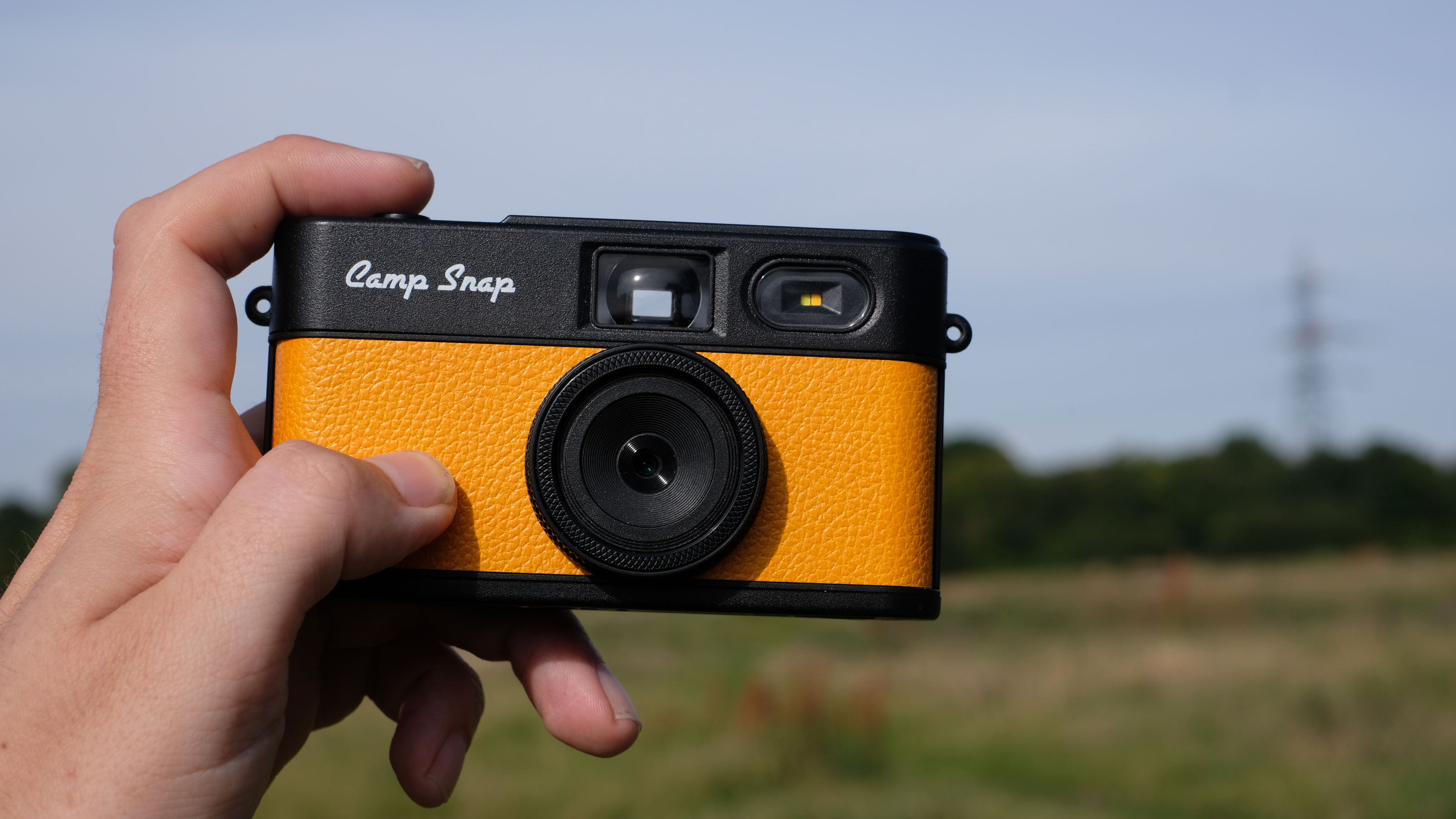 Photograph of man's hand holding Camp Snap 2 digital camera, in yellow colorway