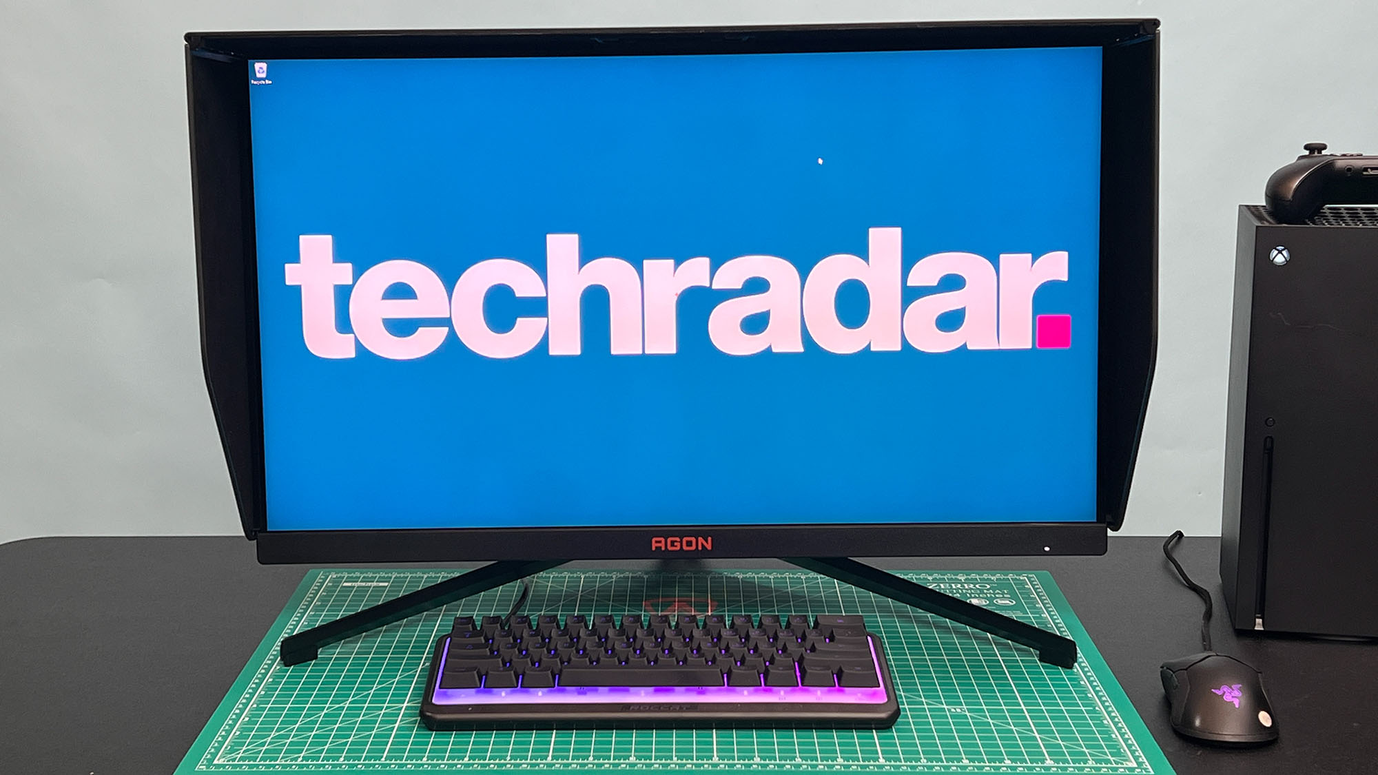 An AOC Agon Pro AG274QZM on a black desk with a green deskmat underneath