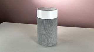The white and gray Blueair Blue Pure Mini Max sits on a pale surface in front of a pink background.