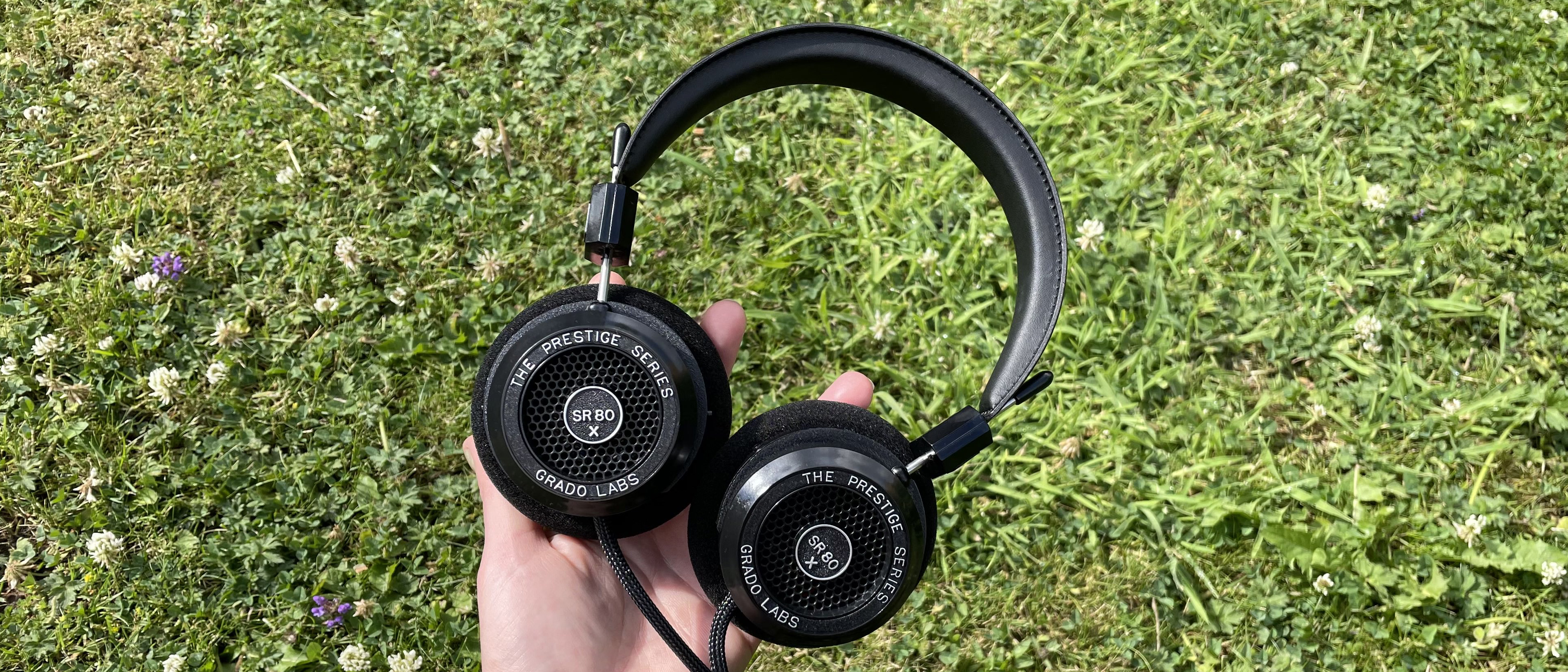 Becca's hand holding the Grado SR80x headphones against some grass
