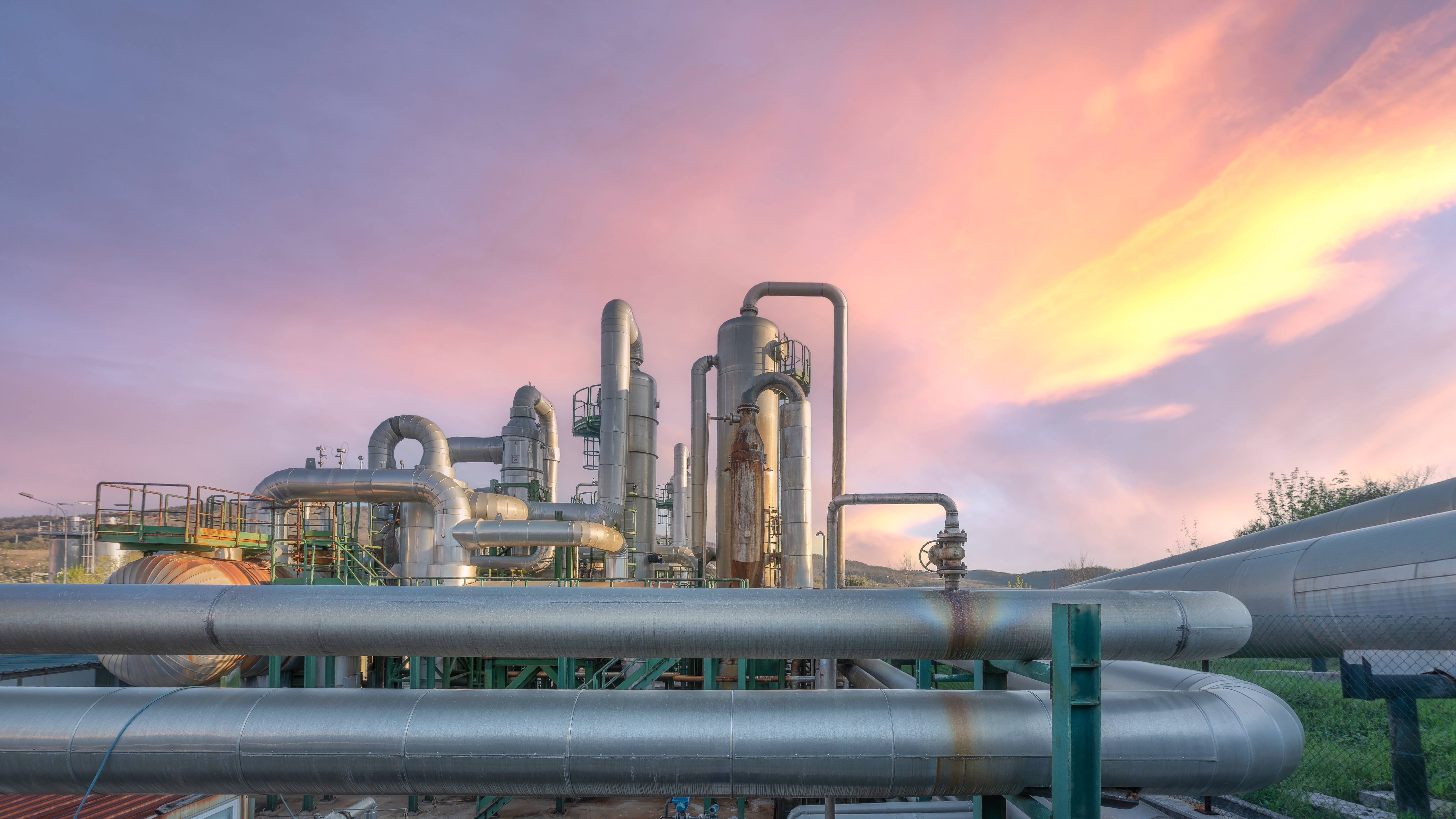Industrial geothermal power plant pipelines at sunset in Larderello, Tuscany region. Steam pipes and equipment for renewable energy production with dramatic pink sky.