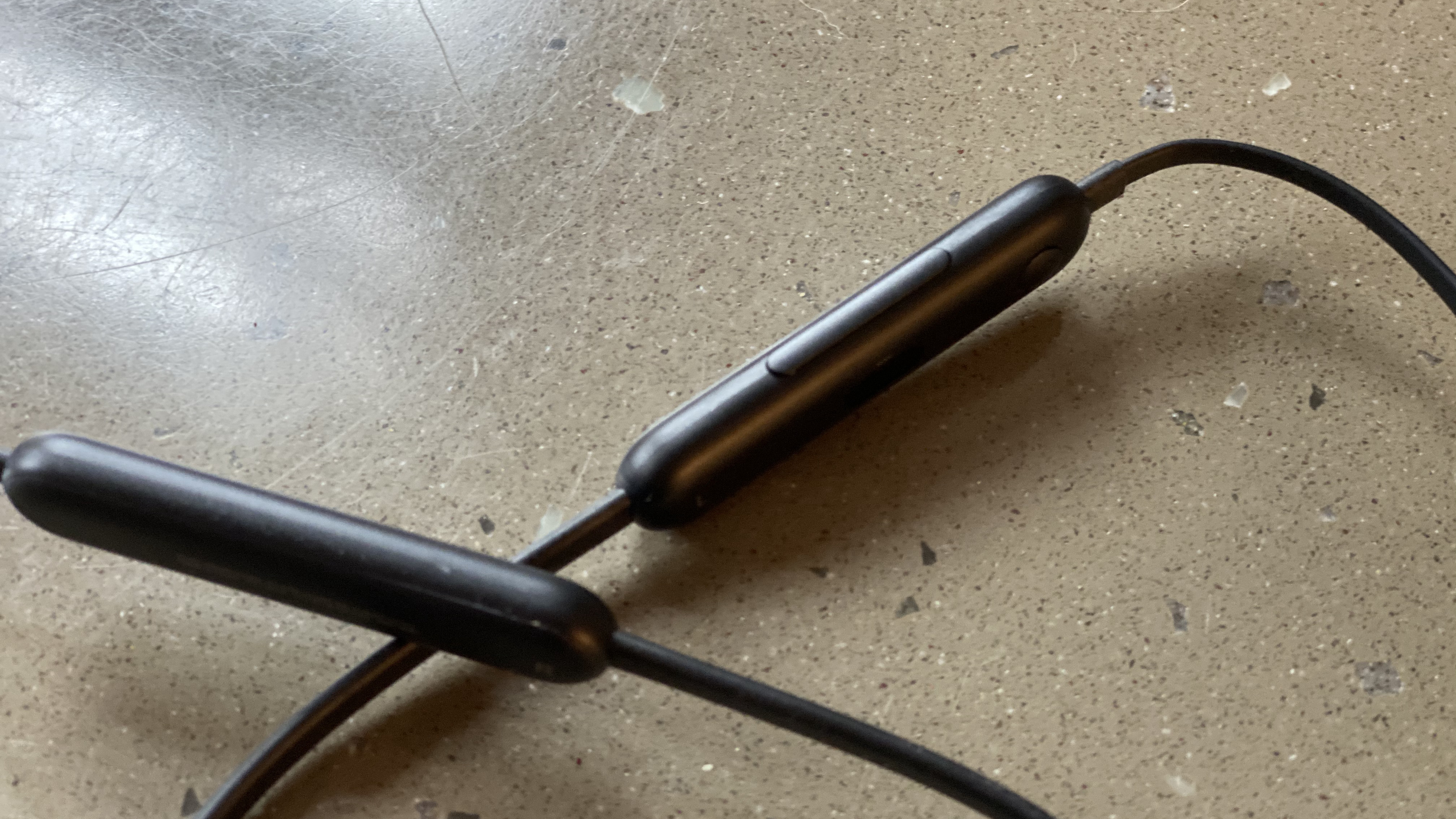 A close up of the controls of the Beats Flex wireless earphones in black on a marble surface