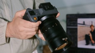 A Hasselblad camera in photographer's hands, alongside a Macbook with the Capture One software on the display