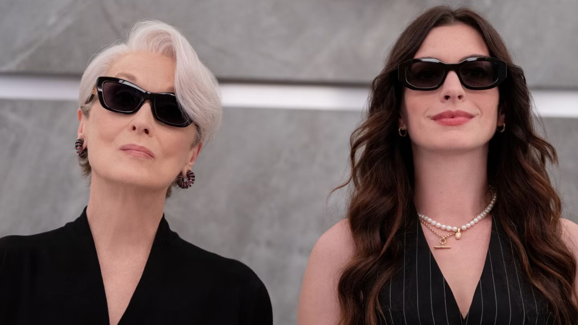 Miranda and Andy stand side by side wearing sunglasses