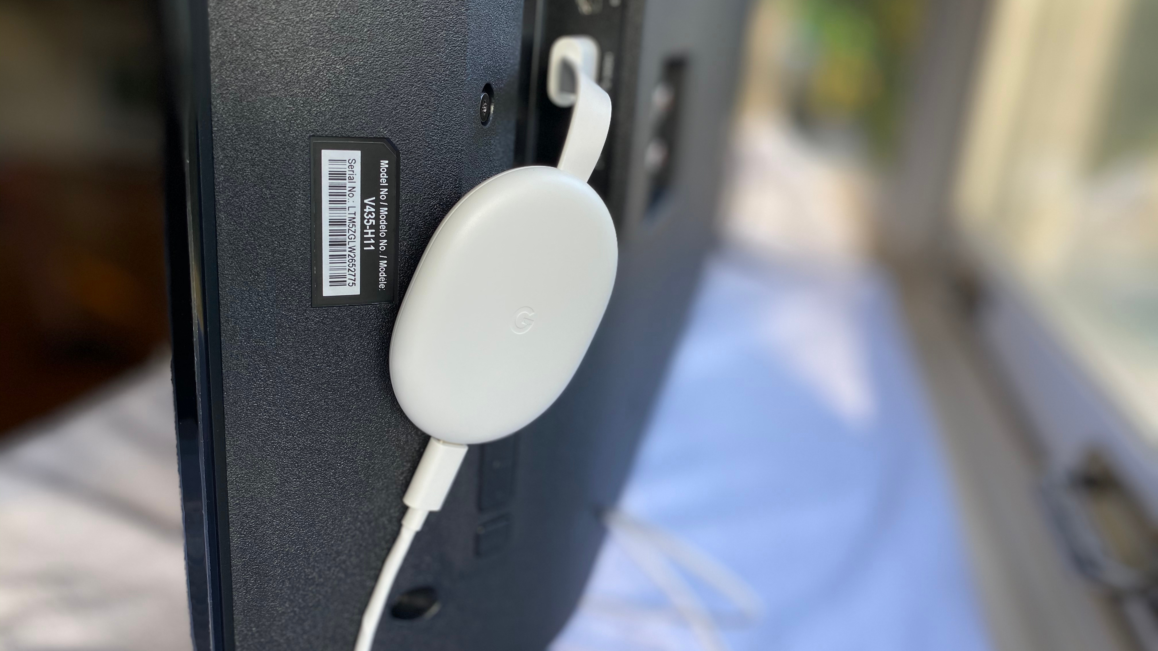 A white chromecast with google tv plugged into the back of a TV set.