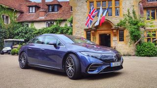 A side view, from the front, of a blue Mercedes-Benz EQS in a manor house car park