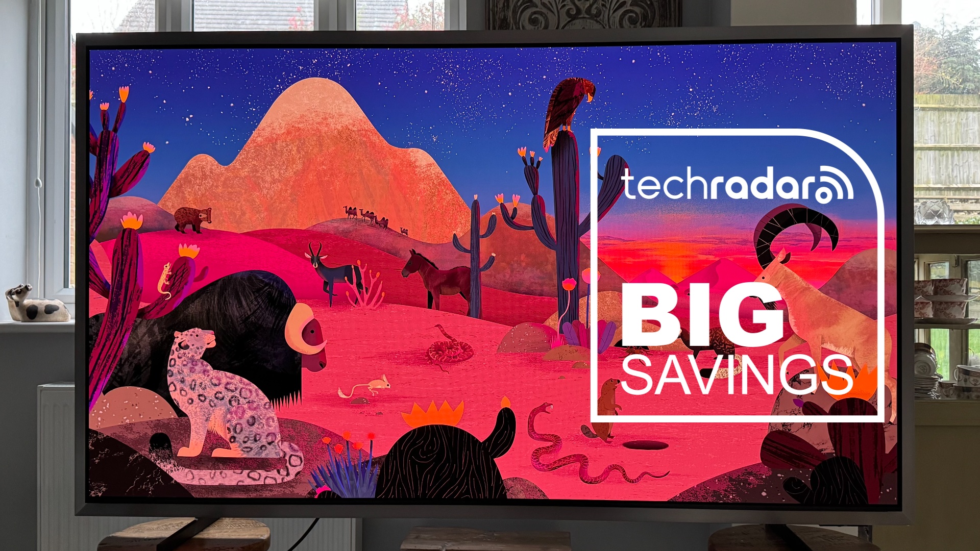 Samsung S95H TV on desk displaying a cartoon scene, with a TechRadar big savings text overlay