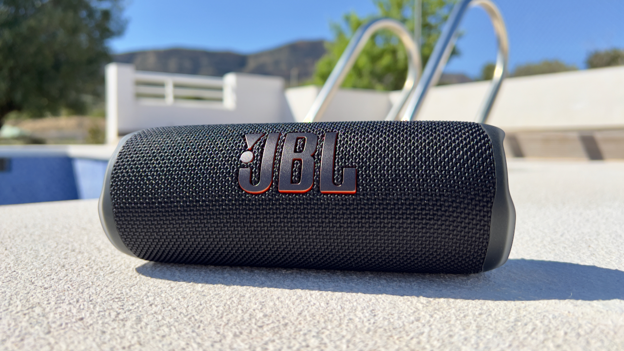 The JBL Flip 6 portable speaker in black pictured next to a swimming pool in bright sunshine.