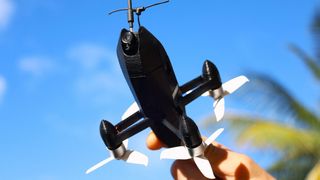 The ESP32 self build rocket drone being held up, with a blue sky and palm tree backdrop
