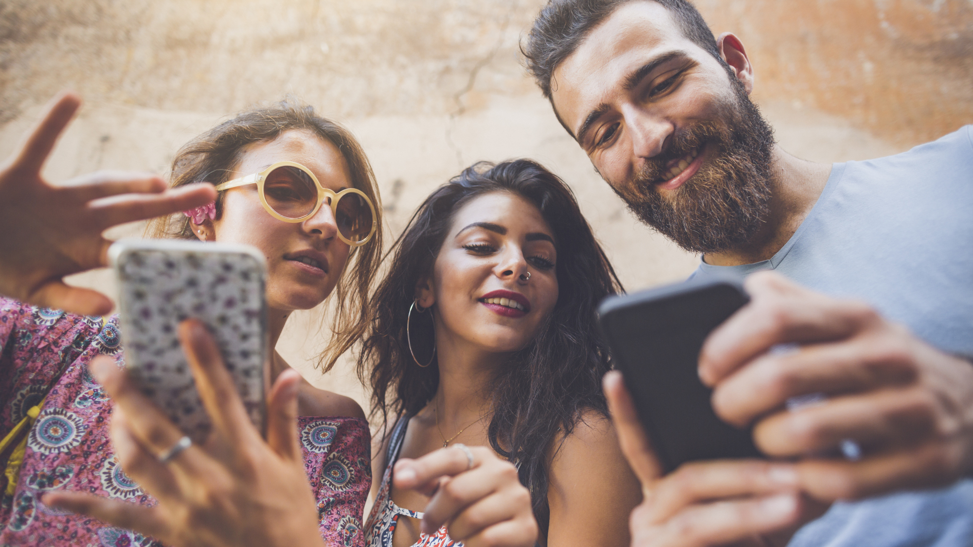 Three people talking together, two of them using their phones