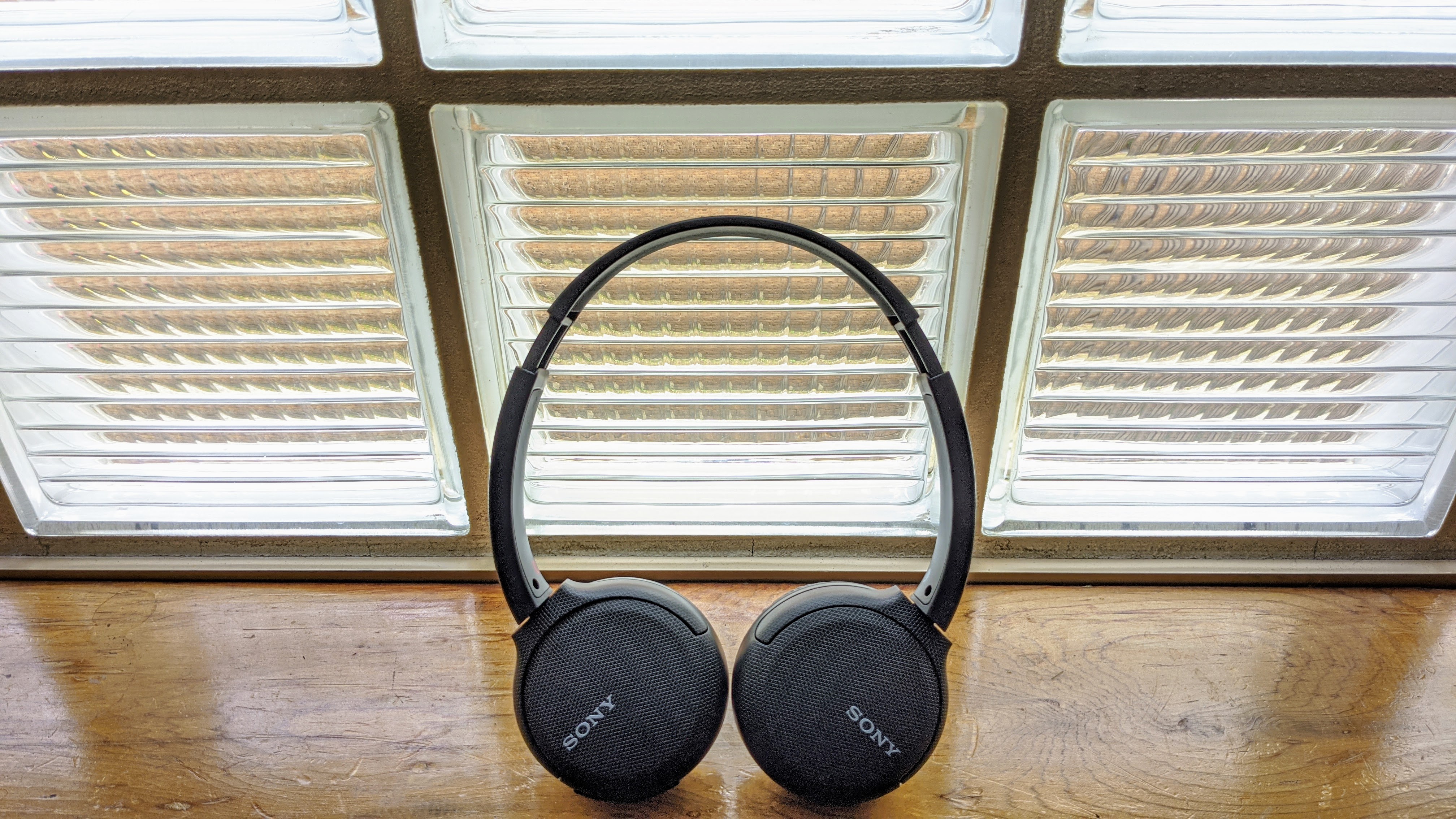 A pair of the Sony WH-CH510 on-ear headphones in black pictured next to a window on a wooden surface