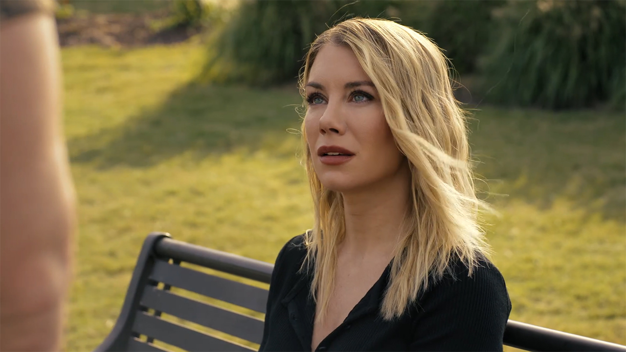 A seated Emilia Harcourt looking up at an off-camera Chris Smith in Peacemaker season 2 episode 5