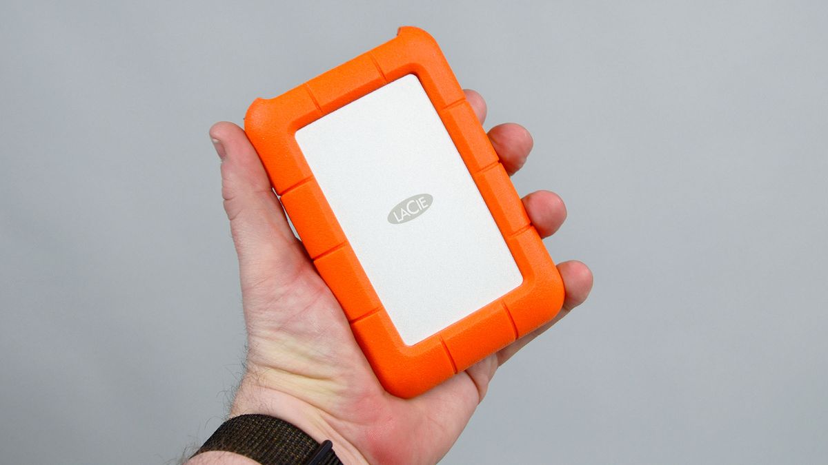 A masculine hand holding a LaCie Rugged Mini external hard drive