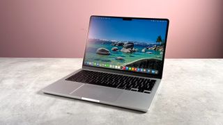 The MacBook Air M5 open 120 degrees and powered on a stone effect surface in front of a pink background.