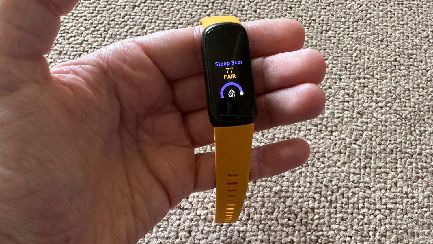 A hand holding a Fitbit Inspire 3 showing a sleep score