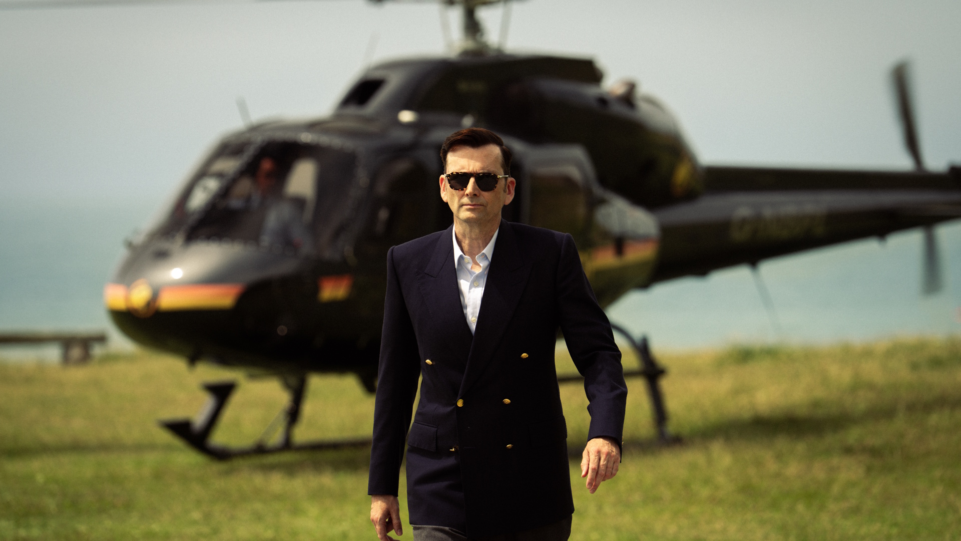 David Tennant as Lord Tony Baddingham standing in front of a helicopter in a scene from Rivals season 2.