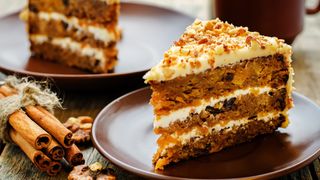 Slice of carrot cake on plates next to a bundle of cinnamon sticks