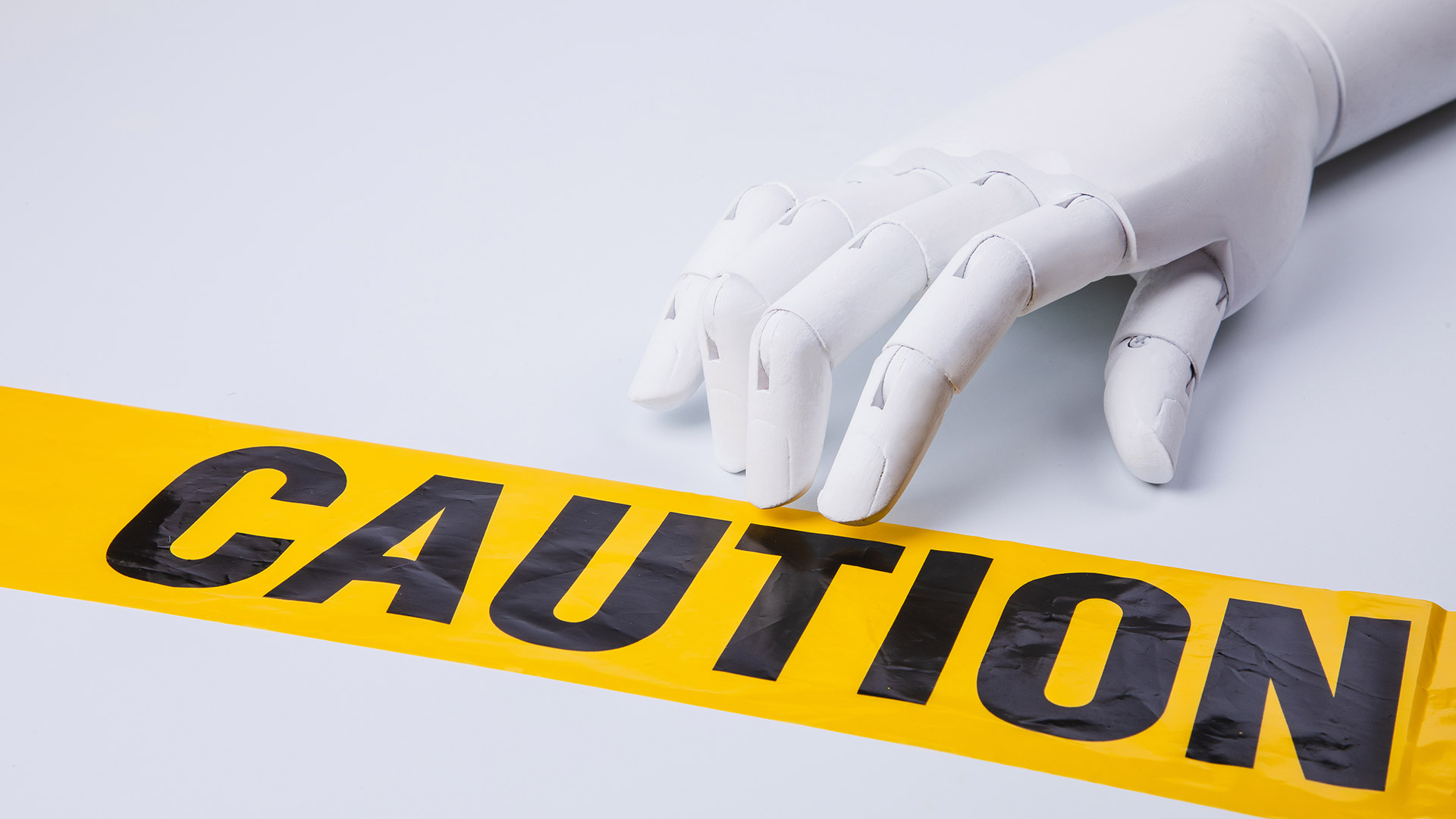 A robot hand reaching towards a yellow sign that reads "Caution" in black letters