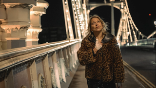 Nicola Walker walks across a bridge wearing a leopard print coat. Her hand is bandaged.