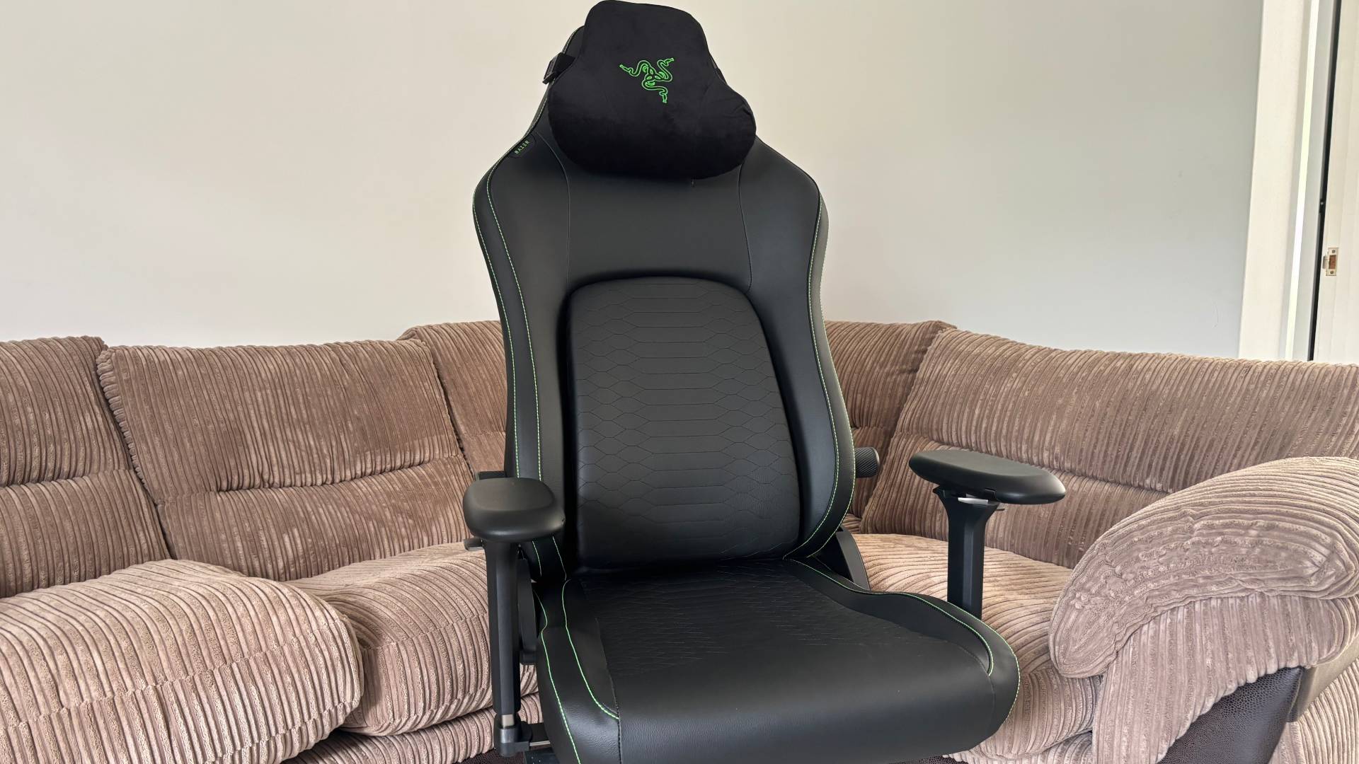 Full Shot of the Razer Iskur V2 NewGen chair against a brown sofa, white hardwood floor, and a white wall in the background. 