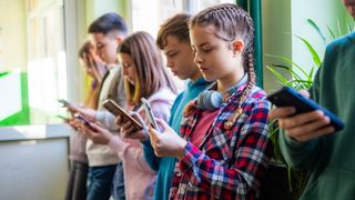 Teenage students are standing in the school hallway, all looking at their phones. - stock photo