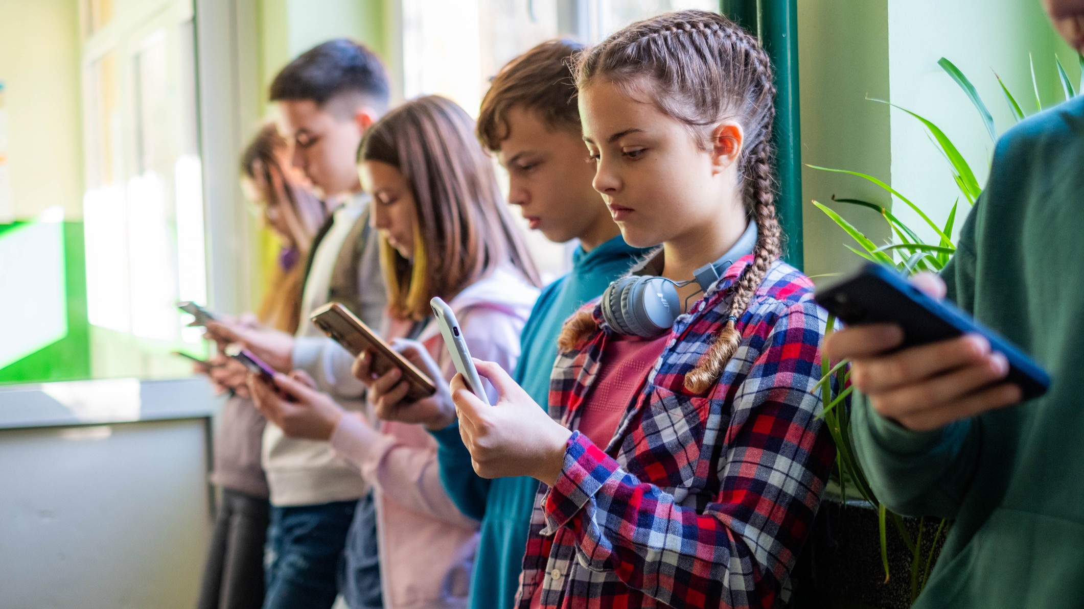 Teenage students are standing in the school hallway, all looking at their phones. - stock photo
