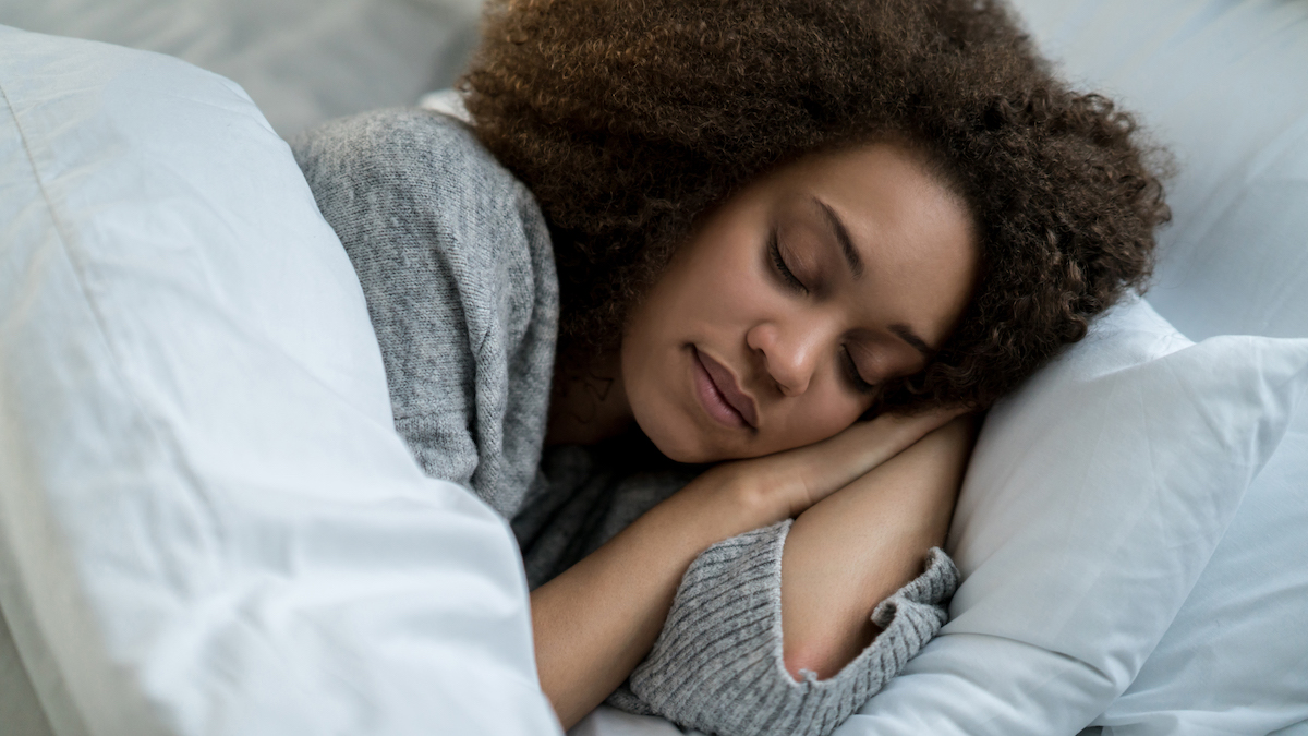 Woman sleeps on her side with her hands tucked under her head place on a comfy white pillow