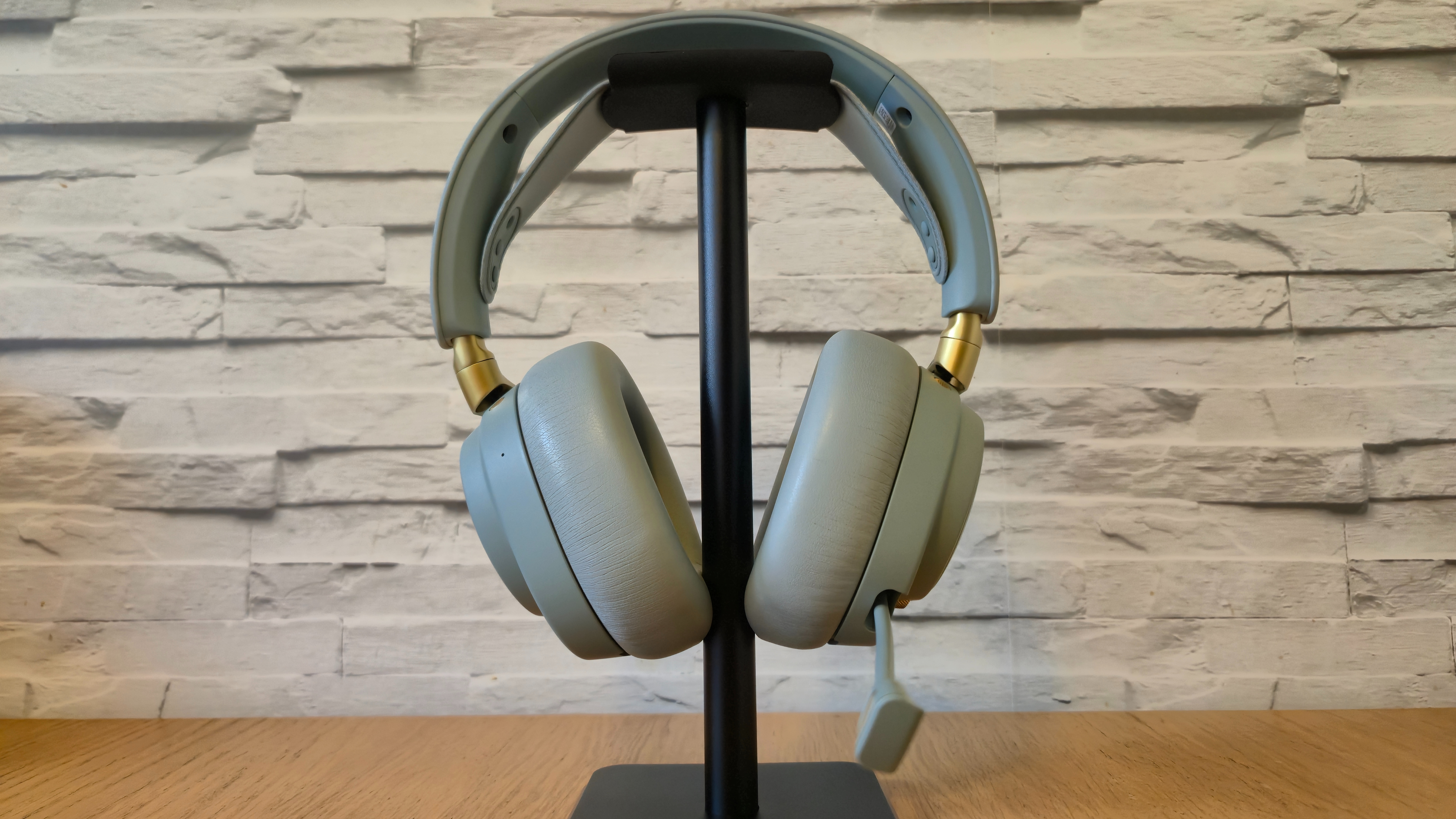 The SteelSeries Arctis Nova Elite headset in front of a white brick background and on a wooden surface