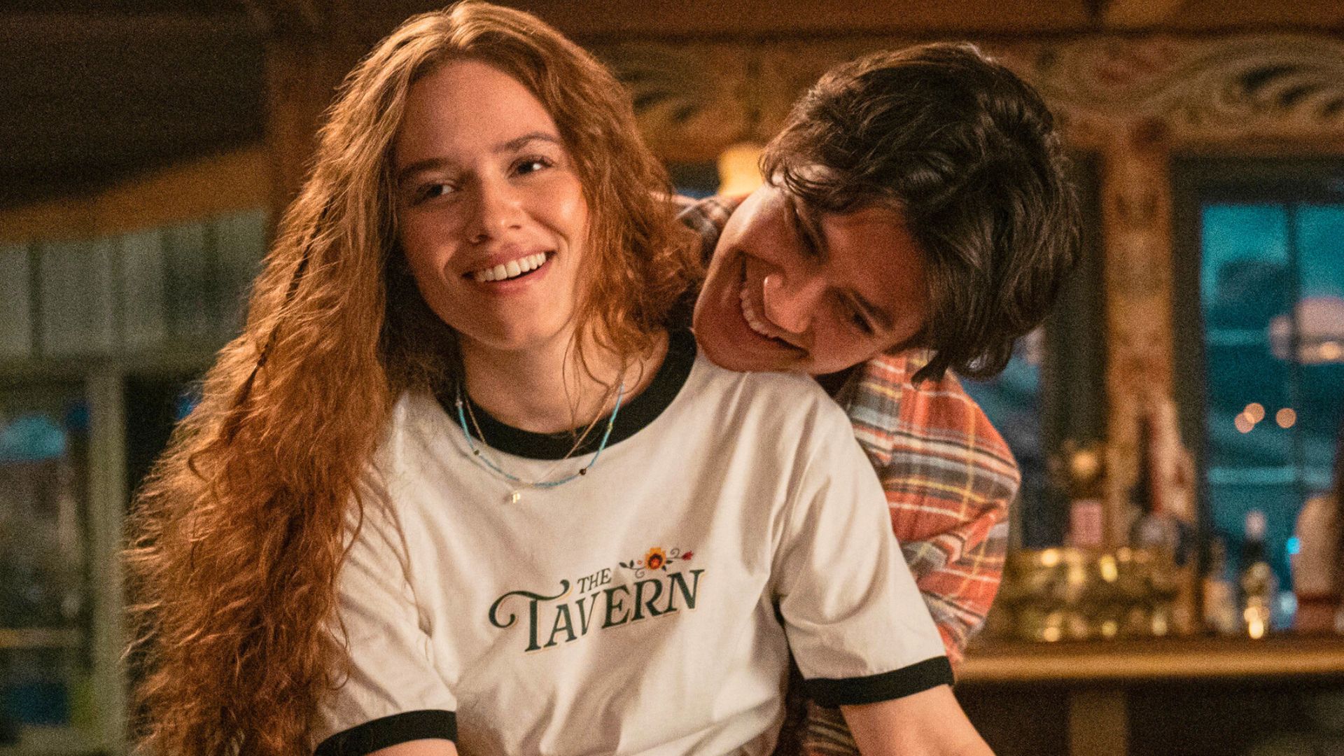 A guy hugs a girl from behind while she smiles