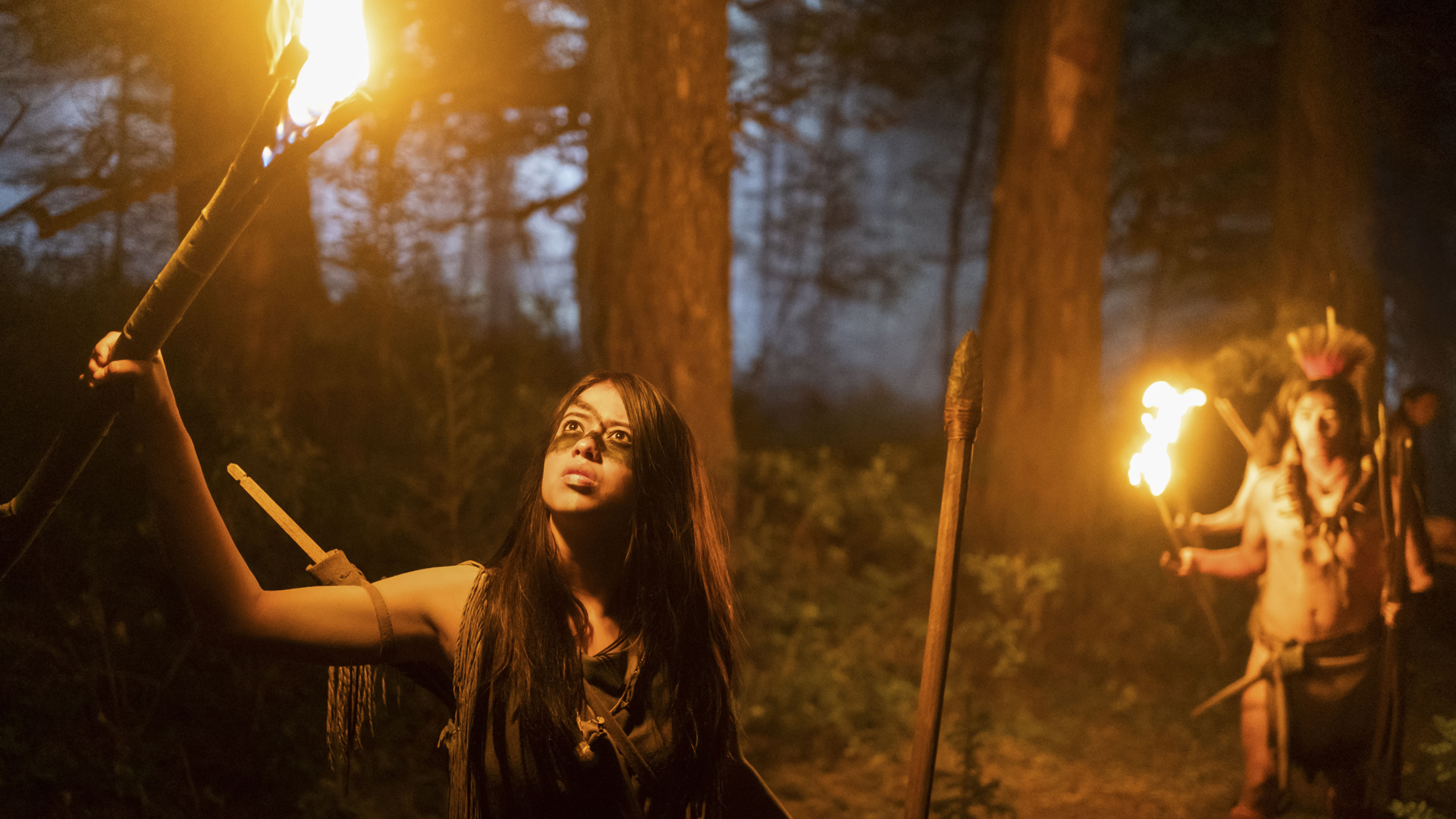 Naru holds a lit torch up to a tree after spotting something in the Hulu/Disney Plus movie Prey