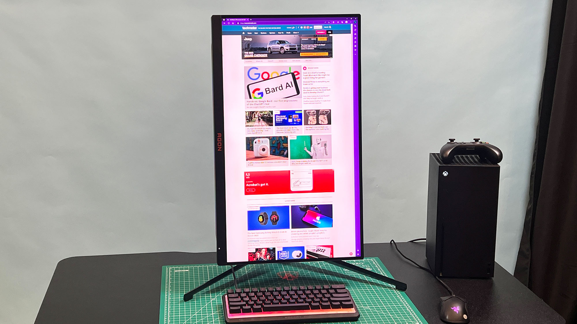 An AOC Agon Pro AG274QZM on a black desk with a green deskmat underneath