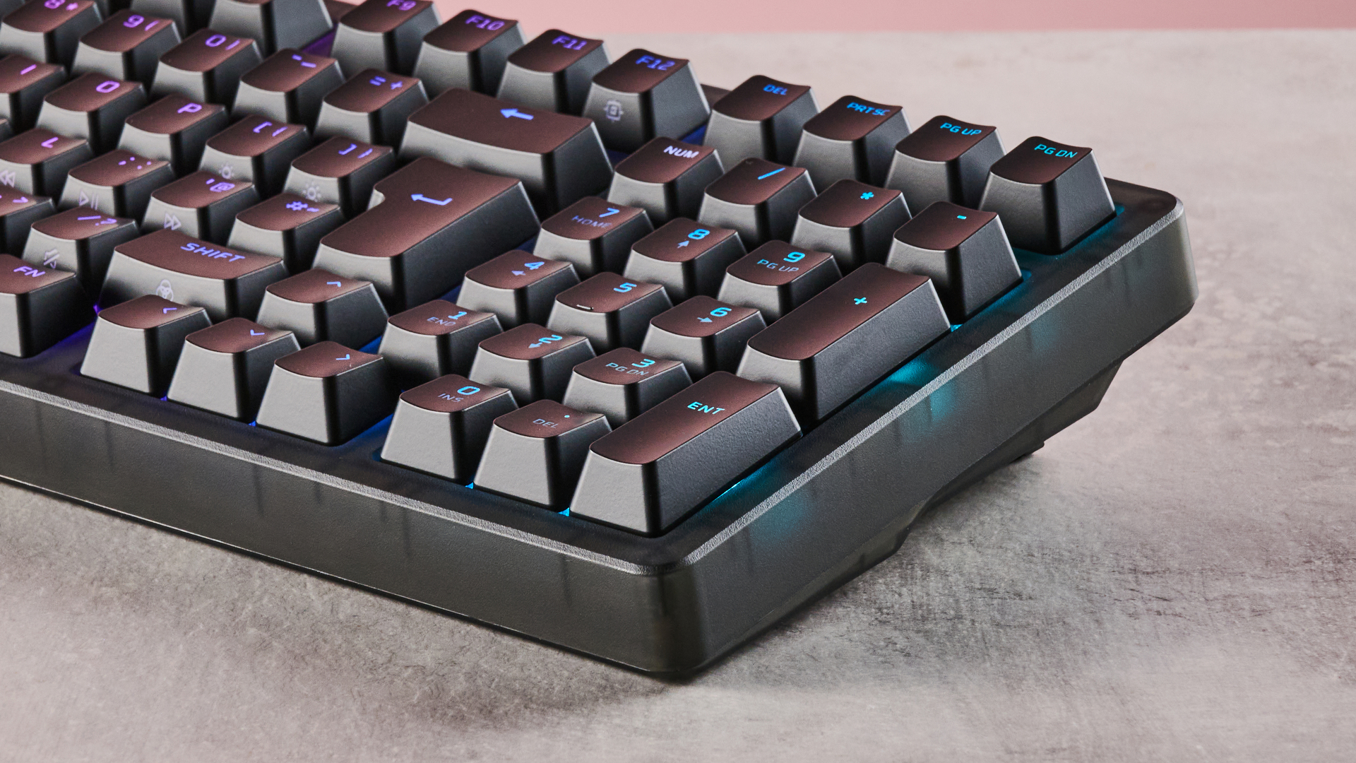 Close-up of right side of HyperX Origins 2 1800, with RGB backlighting on, on a desk with pink wall in background