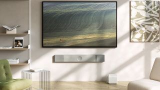 A wall mounted KEF XIO soundbar in grey slate underneath a large TV. The room is in neutral colours and the TV is showing a green landscape.