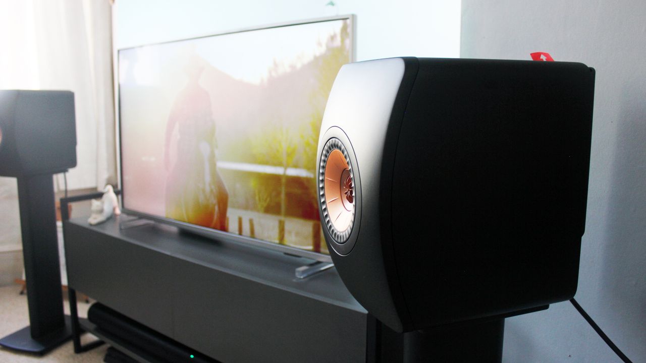 The Kef LS50 speaker shown from an angle. It has a traditional stereo speaker shape, except the front panel is convex, with a circular recess in the center for the speaker driver