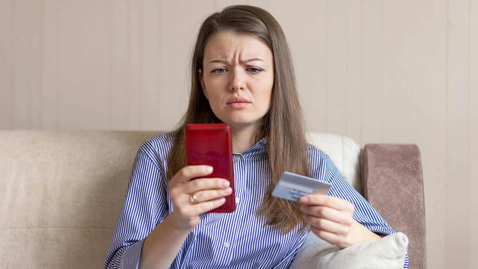 Person using a phone, holding their credit card and looking puzzled over whether something might be a scam