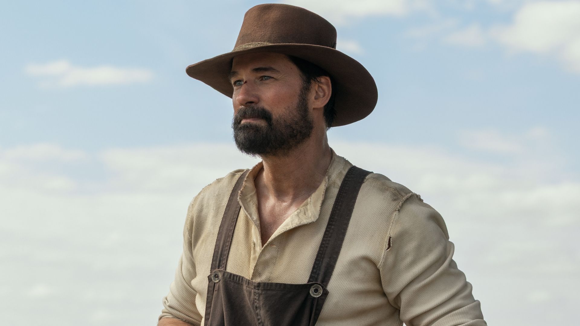 A man in a hat and overalls looks over a field