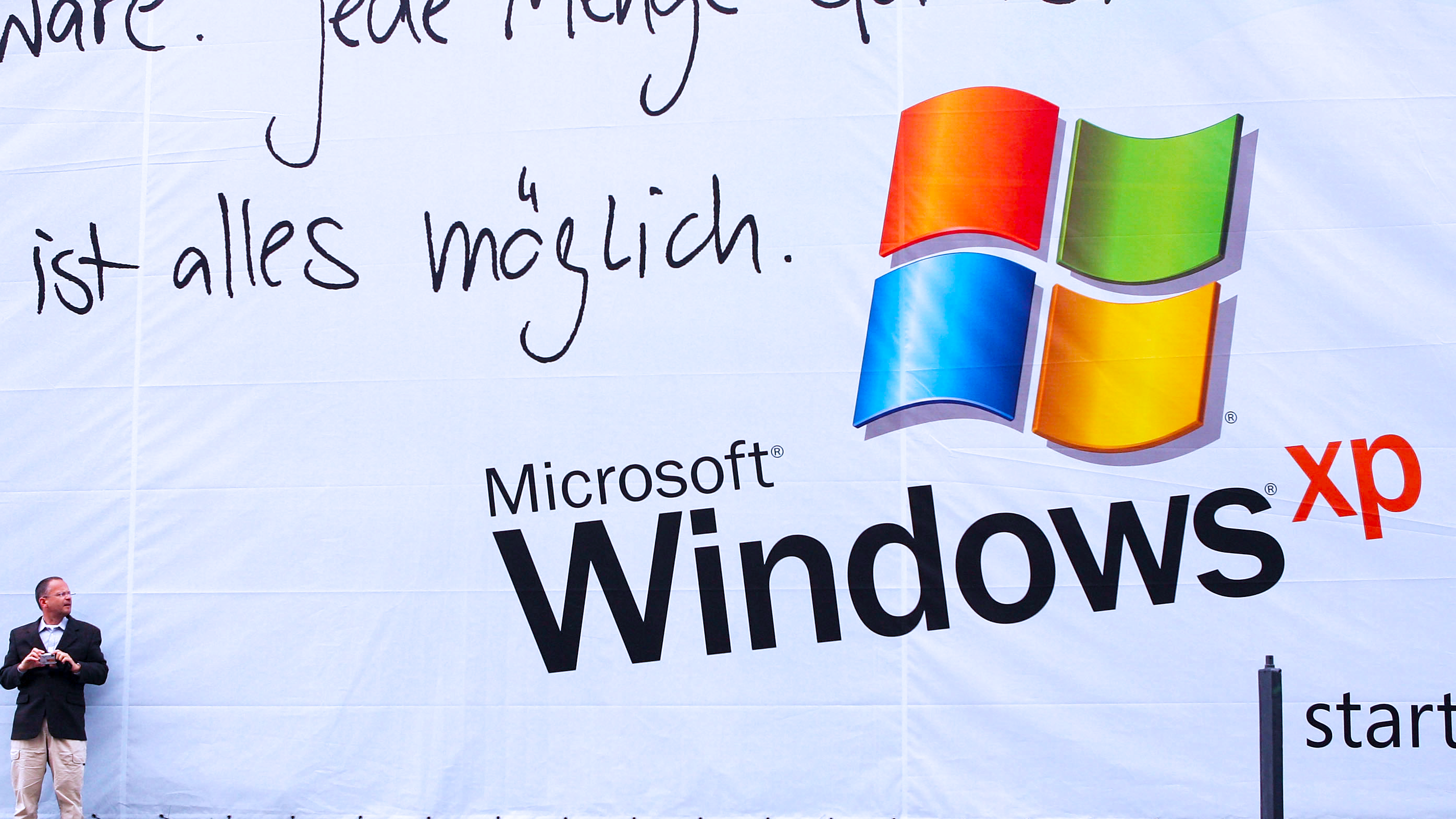 A man with a digital camera prepares to take a picture next to a billboard advertising the Microsoft Windows XP operating system
