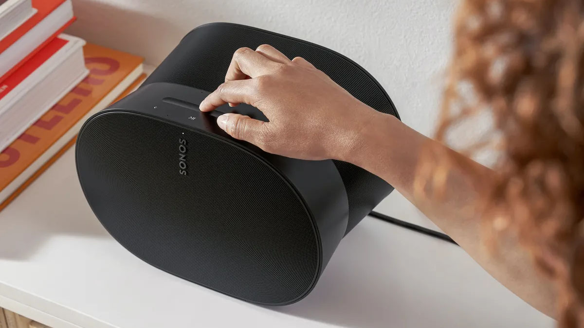 Someone's hand touching the top of a Sonos Era 300 speaker that's sitting on a white surface.