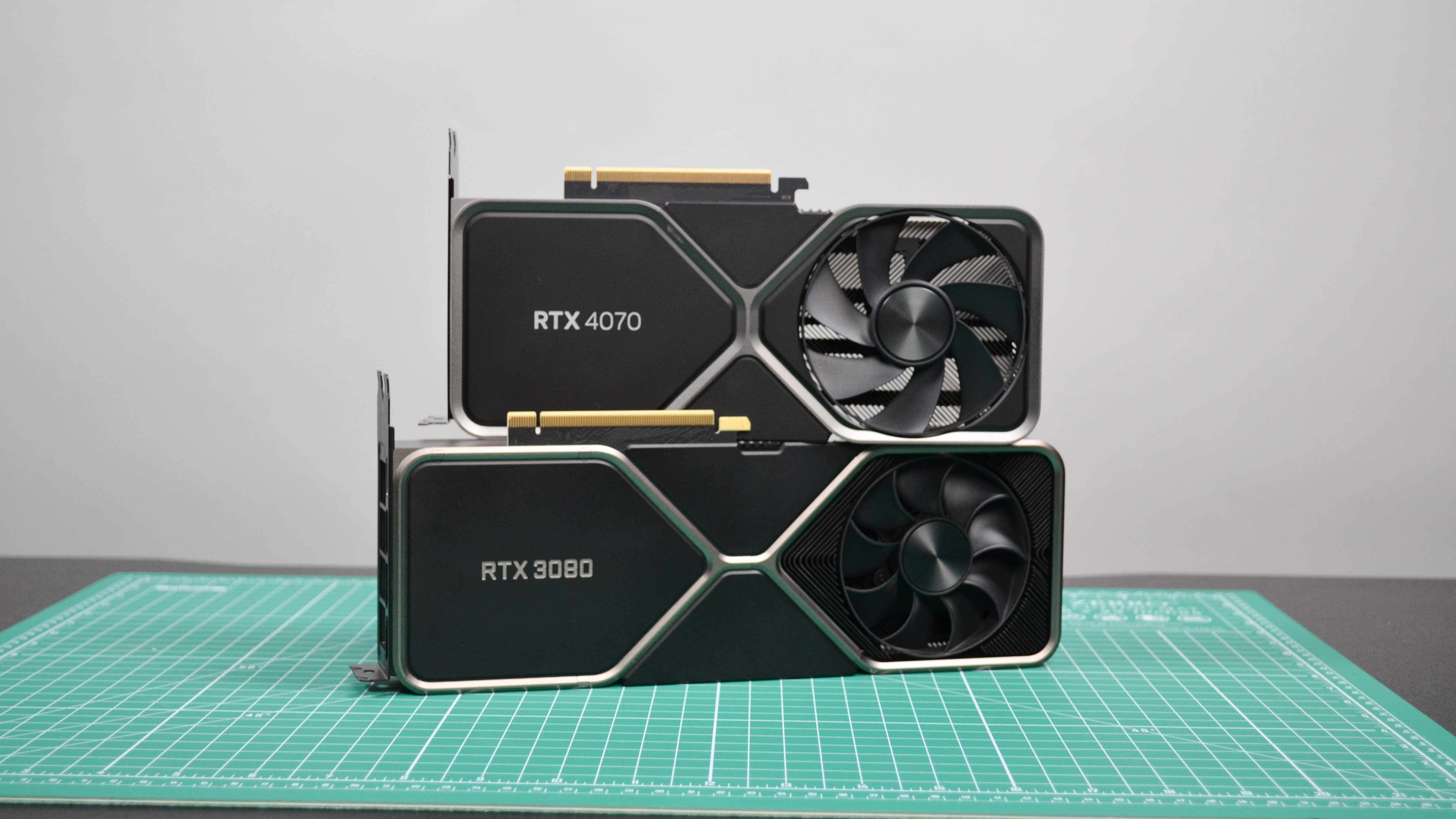 The Nvidia RTX 4070 and RTX 3080 pictured together on a green worksurface.