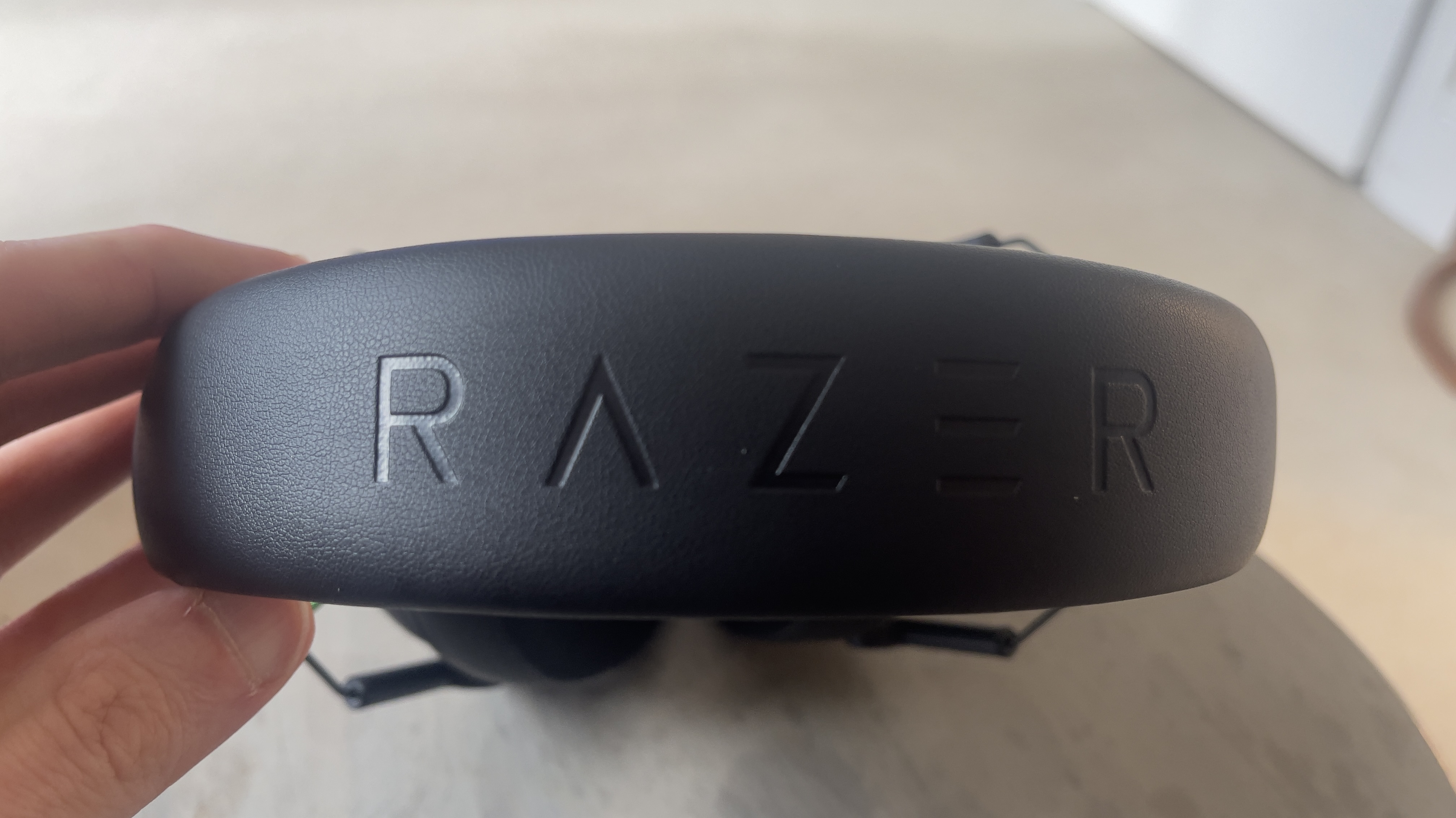 The Razer Blackshark V3 X gaming headset on a table. A living room is visible in the background.