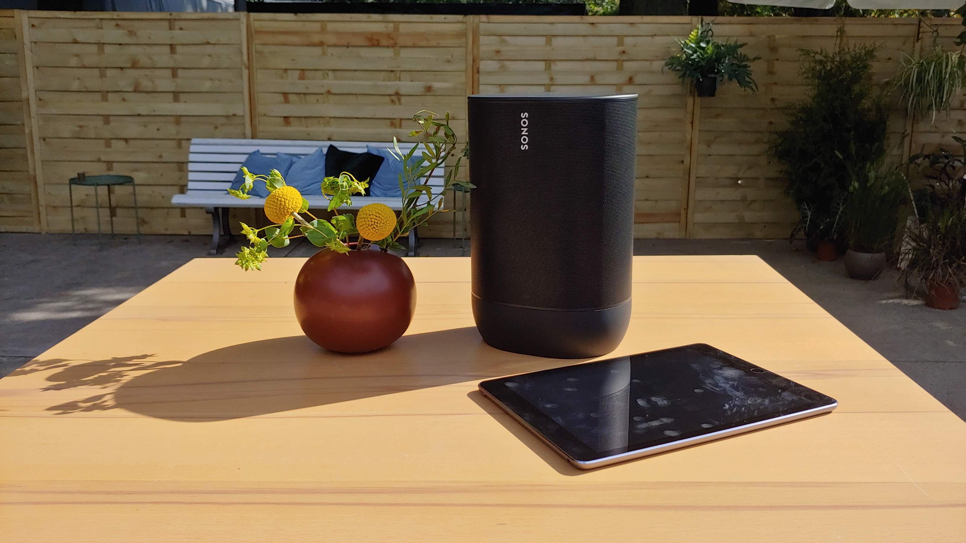 The Sonos Move at a distance pictured on a wooden table next to an iPad