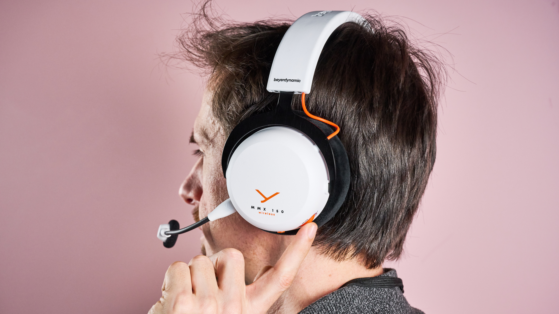 The Beyerdynamic MMX 150 Wireless on a man's head from a rear angle; he is spinning the volume wheel on one earcup with one finger.